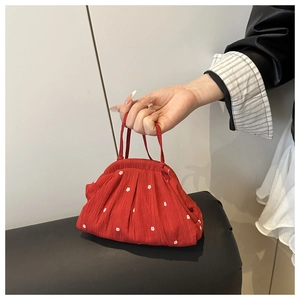 Detail of red floral fabric shell bag with white polka dots held by a hand