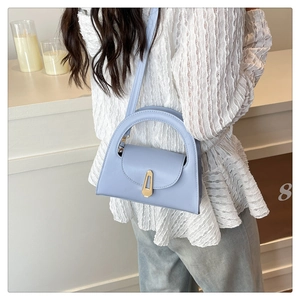 Detail of light blue semi-circular leather handbag with gold geometric clasp on model