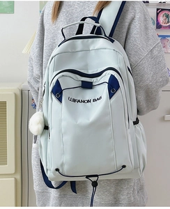 Detail of light blue waterproof nylon backpack with embroidery and plush ball charm