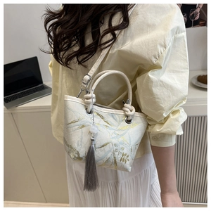 Close-up of cream bucket bag featuring intricate gold and blue leaf embroidery and tassel