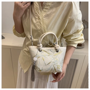 Detail of embroidered bamboo leaves and decorative tassel on a white bucket bag