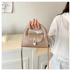 Detail of tan leather crossbody bag with semi-circle handle and gold metal lock clasp