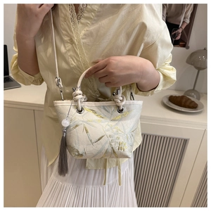 Detail of elegant cream bucket bag with gold bamboo pattern and grey tassel accent
