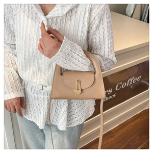 Detail of a beige trapezoid leather handbag with a gold geometric lock and top handle