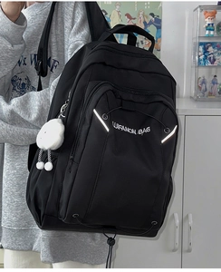 Detail of a black canvas backpack with white logo and decorative plush ball charm