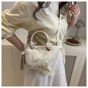 Close-up of off-white tote with leaf embroidery, tassel charm and crossbody strap