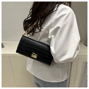 Vista laterale di una borsa a spalla nera coccodrillo con catena dorata su modella