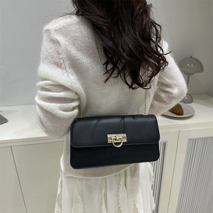 Minimalist black leather crossbody bag with golden horseshoe clasp worn by a model
