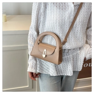 Minimalist light brown structured handbag with round handle and gold clasp on a model