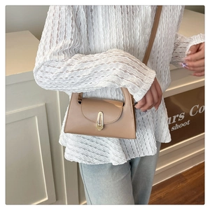 Detail of brown leather crossbody bag featuring a golden geometric clasp and slim strap