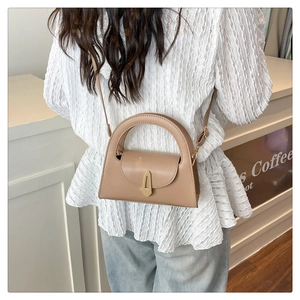Detail of warm khaki crossbody bag with semi-circular handle and gold clasp on model