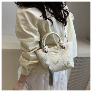 Detail shot of a beige canvas bucket bag with green leaf pattern and beaded tassel charm