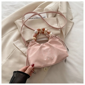 Detailed view of pink drawstring bucket bag with amber beaded handle and brand print