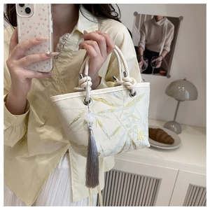 Detail of cream bucket bag with bamboo leaf pattern and woven rope handle and tassel