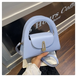 Detail view of light blue leather handbag featuring golden metal buckle and top handle