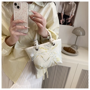 Detail of off-white bucket bag with leaf embroidery and elegant grey tassel pendant