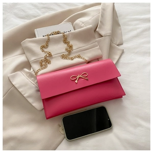 Detail of rose pink leather envelope bag featuring a golden bow buckle and chain strap