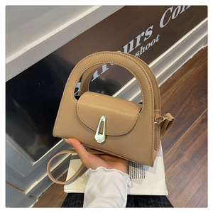 Detail view of structured beige handbag featuring a large circular handle and silver geometric lock