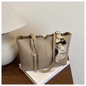 Detail of khaki tote bag with V-cut edge and decorative silk scarf on minimalist background
