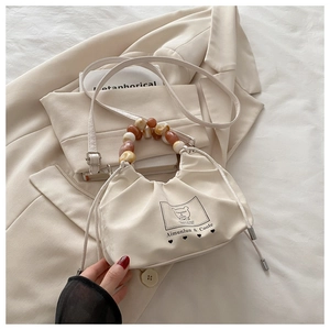 Detail of cream pleated bucket bag with vintage beaded handle and bear graphic