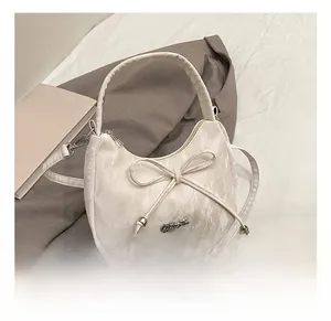 Détail du sac à bandoulière blanc avec nœud, texture moirée et logo argenté