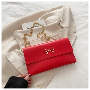 Detail of red envelope bag featuring a gold bow buckle on beige blazer background