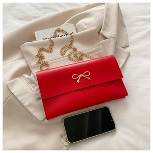 Close-up of bright red envelope chain bag with golden bow hardware on a beige blazer