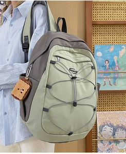 Détail d'un grand sac à dos en nylon bicolore avec cordons élastiques et pendentif biscuit