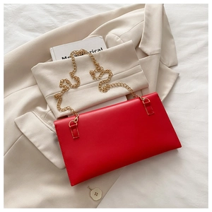 Close-up of a red envelope clutch bag with gold chain strap on a stylish blazer background