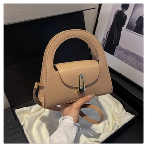 Detail of minimalist beige semi-circle handbag with golden geometric clasp in a gift box