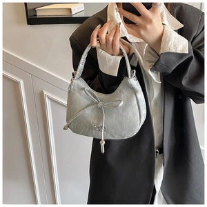 Detail of silver crescent underarm bag with pleated texture and stylish metallic bow