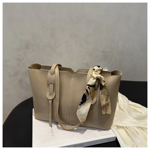 Detail of a beige leather tote bag featuring a decorative silk scarf and V-cut design
