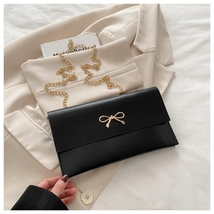 Detail of black envelope clutch with gold bow clasp on beige blazer background
