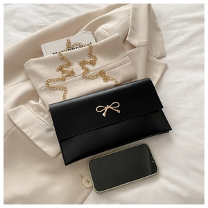 Close-up of black envelope bag with gold bow clasp and metal chain on a beige blazer