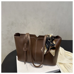 Detail of dark brown leather tote bag featuring contrast stitching and a patterned silk scarf