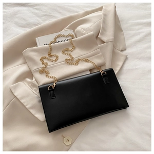 Minimalist black envelope bag with pale gold chain strap on a white blazer