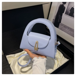 Detail of light blue semi-circular handbag with gold clasp in luxury gift box