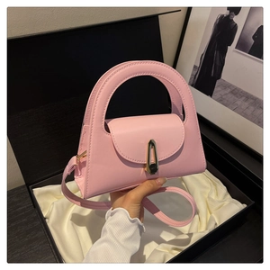 Detailed view of pink semi-circular handbag with gold clasp on beige silk and gift box