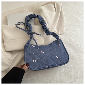 Détail du sac bandoulière en jean bleu avec broderie nœud rose et bandoulière plissée