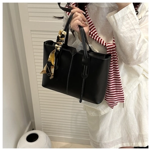 Detail of black leather tote bag with white contrast stitching and decorative scarf handle