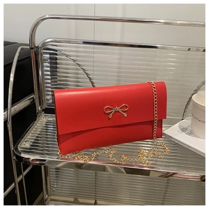 Detail of red envelope bag with gold bow clasp and chain strap on a modern display