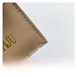 Detail of premium beige pebbled leather texture with precise stitching and gold logo