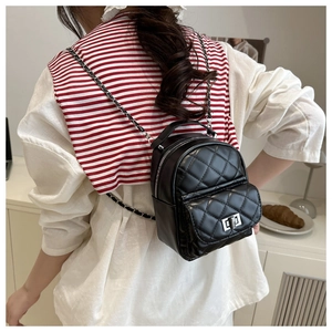 Detail of a black quilted mini backpack featuring silver chain straps and turn-lock