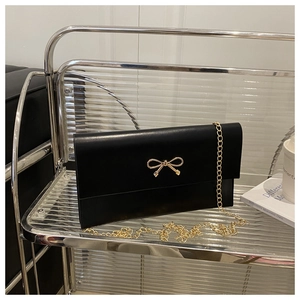 Detail of black matte envelope bag with a gold metal bow clasp and chain strap