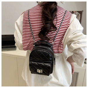 Detail of black quilted mini backpack featuring a silver twist lock and chain strap