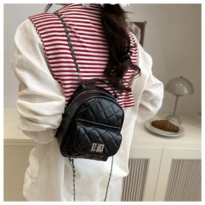 Detail of black quilted mini backpack with silver twist lock and woven chain strap on model