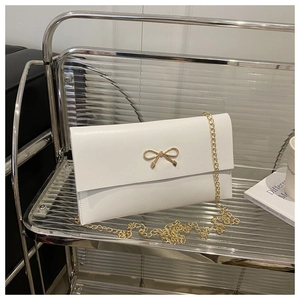 Detail of white envelope bag with gold bow clasp and sleek metal chain strap