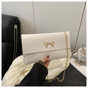 Detail of white envelope clutch bag with golden metal bow accent and chain strap