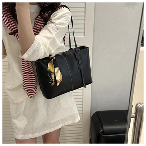 Detail of a black leather tote bag with white stitching and yellow silk scarf handle