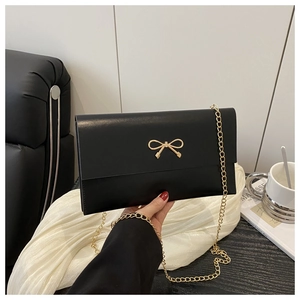 Detail of black envelope bag featuring golden bow clasp and slender metal chain strap